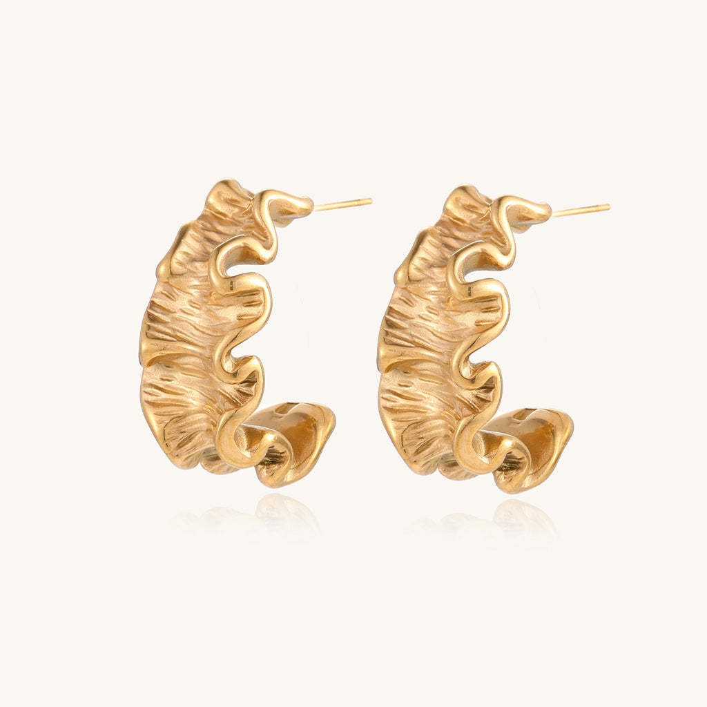 Textured gold-plated hoop earrings with wavy sculptural ridges displayed against a neutral background.